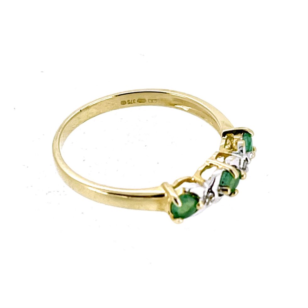 Detailed view of the yellow gold claw settings holding three round-cut emerald gemstones