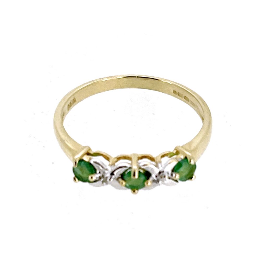 Close-up of three green emeralds separated by two diamonds in a traditional five-stone arrangement